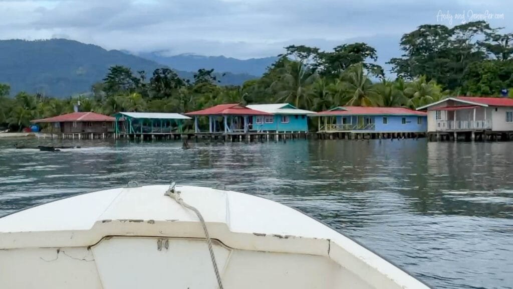 Boat approaching a waterfront village near Bocas del Toro, Panama, with rainforest-covered mountains beyond.