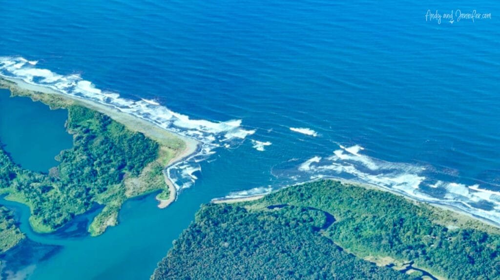 An aerial view of Panama's Caribbean coastline shows rainforest, river mouths and reefs meeting the deep blue sea, with waves breaking along the shoreline.