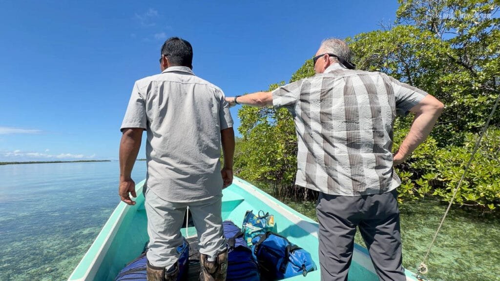 A local guide and a traveler stand in the bow of a small boat navigating crystal-clear Caribbean waters through mangroves near Bird Island in Bocas del Toro, Panama.
