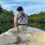 Guide riding at the bow of a boat through calm mangrove-lined waterways near Isla Popa, Bocas del Toro, Panama.