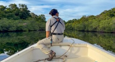 Guide riding at the bow of a boat through calm mangrove-lined waterways near Isla Popa, Bocas del Toro, Panama.