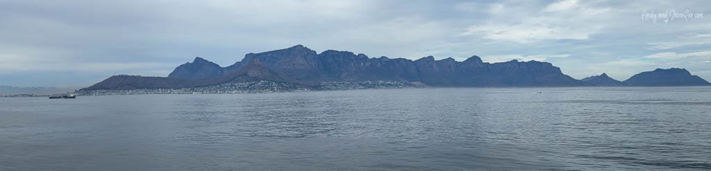 Cape Town beneath Table Mountain, Lion’s Head and Signal Hill, viewed across Table Bay under cloudy skies.