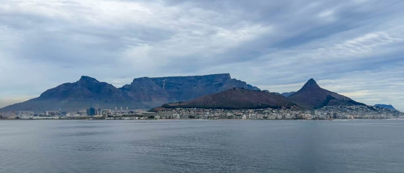 Cape Town beneath Table Mountain, Lion’s Head and Signal Hill, viewed across Table Bay under cloudy skies.
