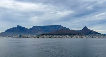 Cape Town beneath Table Mountain, Lion’s Head and Signal Hill, viewed across Table Bay under cloudy skies.