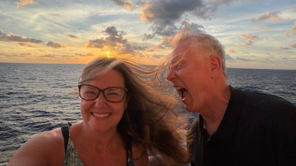 Andy trying to eat Jennifer's hair being blown in the wind as they take a selfie at sunset on the Norwegian Spirit